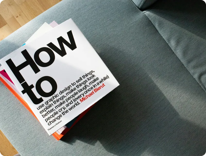 Stack of “How to” books by Michael Bierut lying on a grey sofa