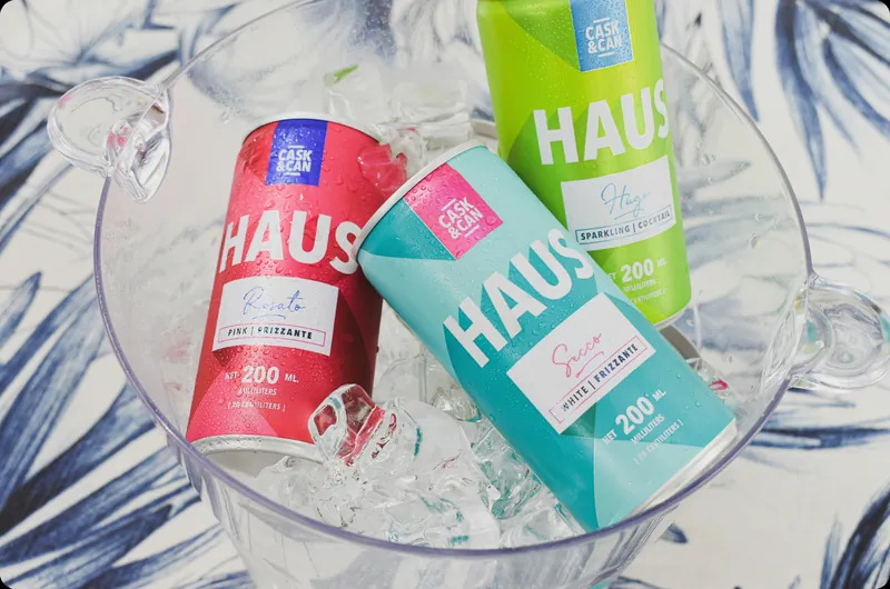 Three Haus sparkling wine cans in pink, teal and green on ice in a glass bowl