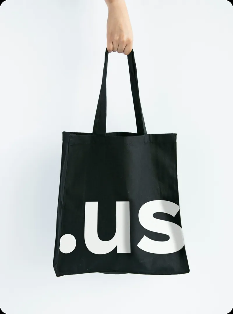Hand holding a black tote bag printed with a large white “.us”